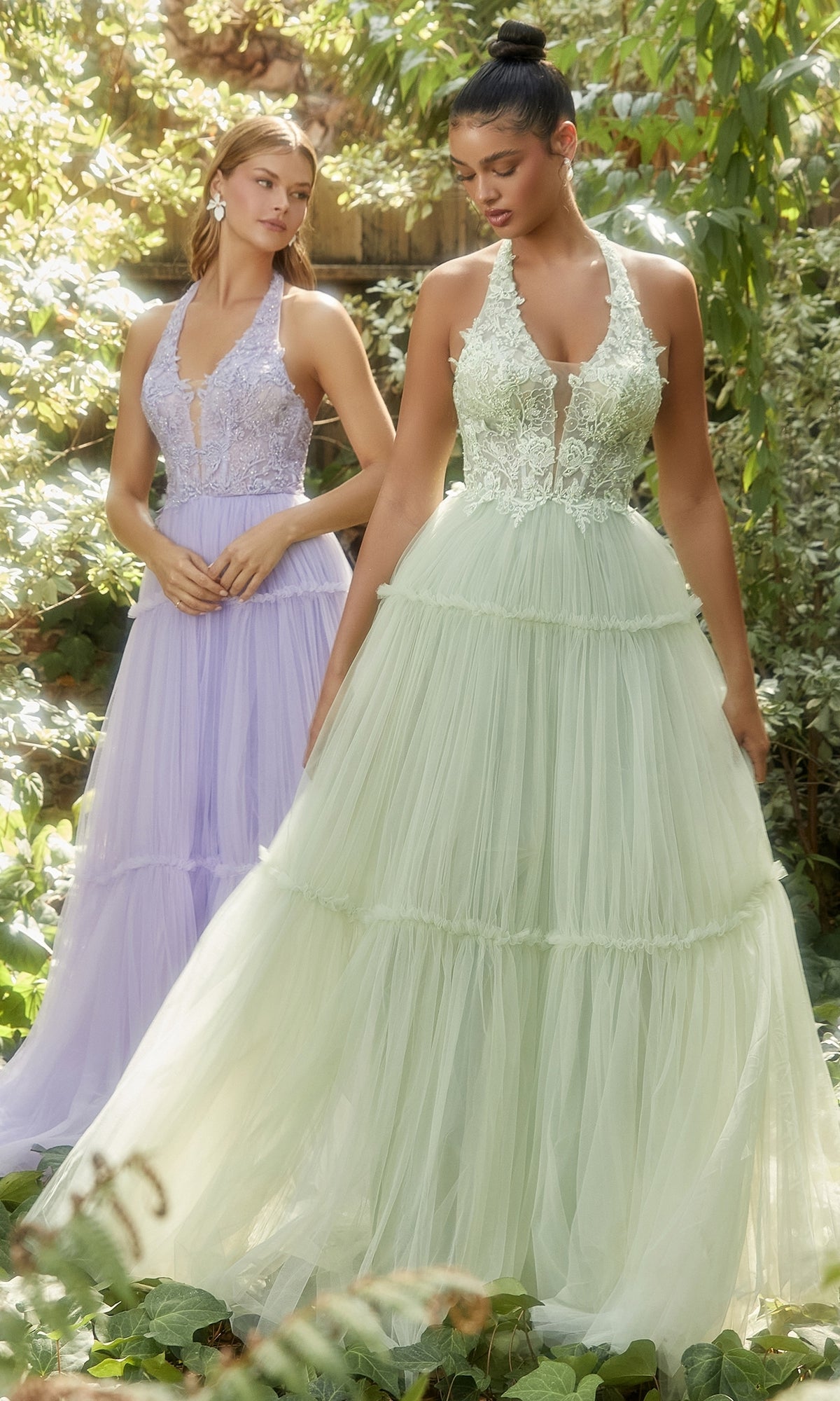 Two women wear floor-length sleeveless tulle gowns outdoors, one in pale lavender, the other light green. The lavender dress is the Lace-Halter Long A-Line Prom Dress A1206. They are surrounded by lush greenery.